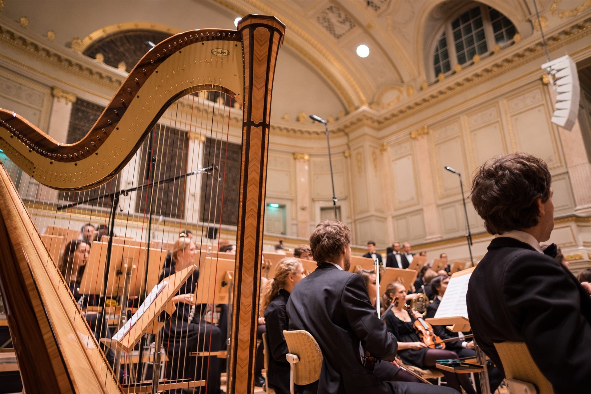A harp on a concert-hall stage with an orchestra
